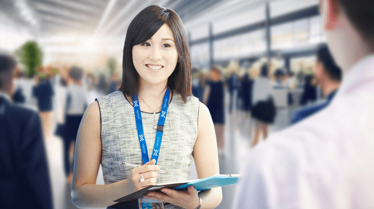 A business exhibitor with a lanyard and clipboard ready to show off the company offerings and form partnerships in a busy crowd